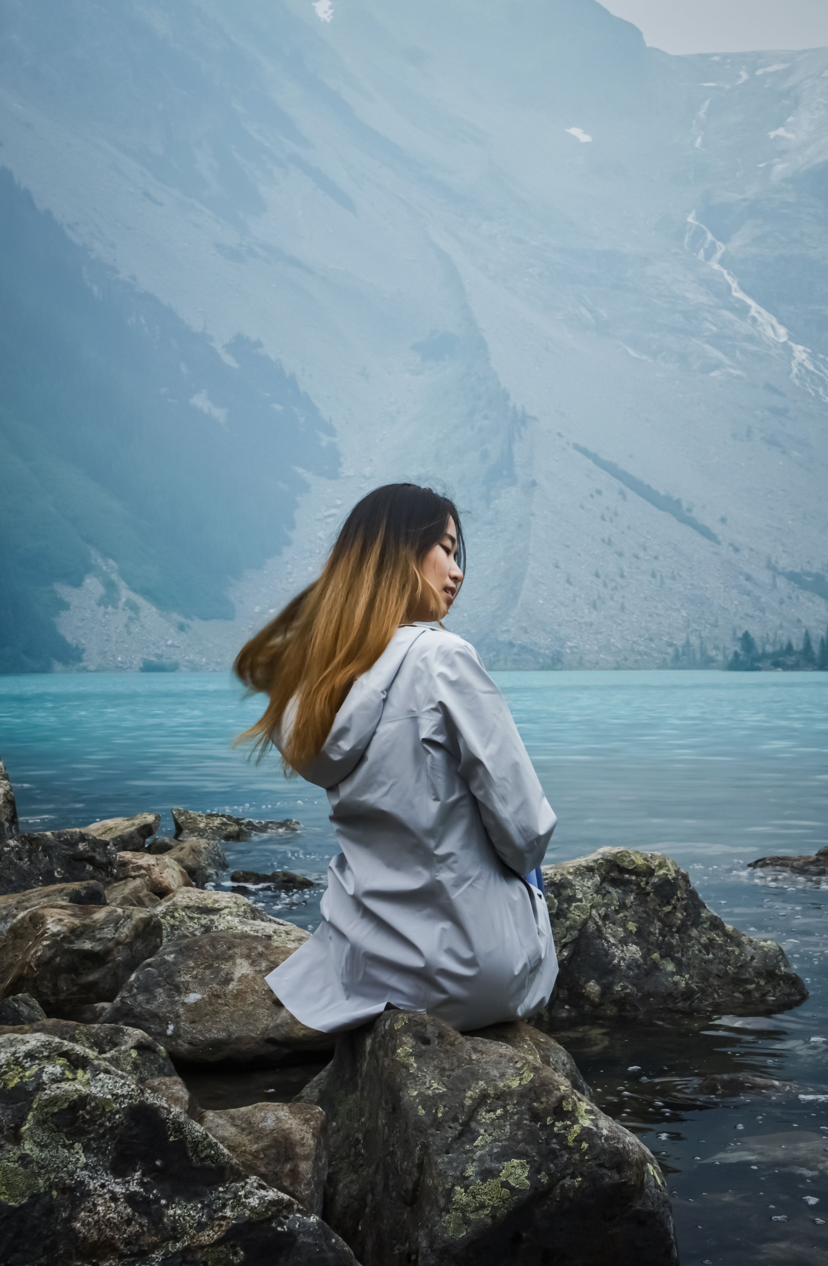 Woman in Gray Long Sleeve Shirt Sitting on Rocky Shore · Free Stock Photo