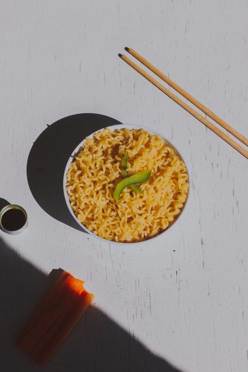 Free Flat lay of a bowl of noodles garnished with vegetables, accompanied by chopsticks on a white background. Stock Photo