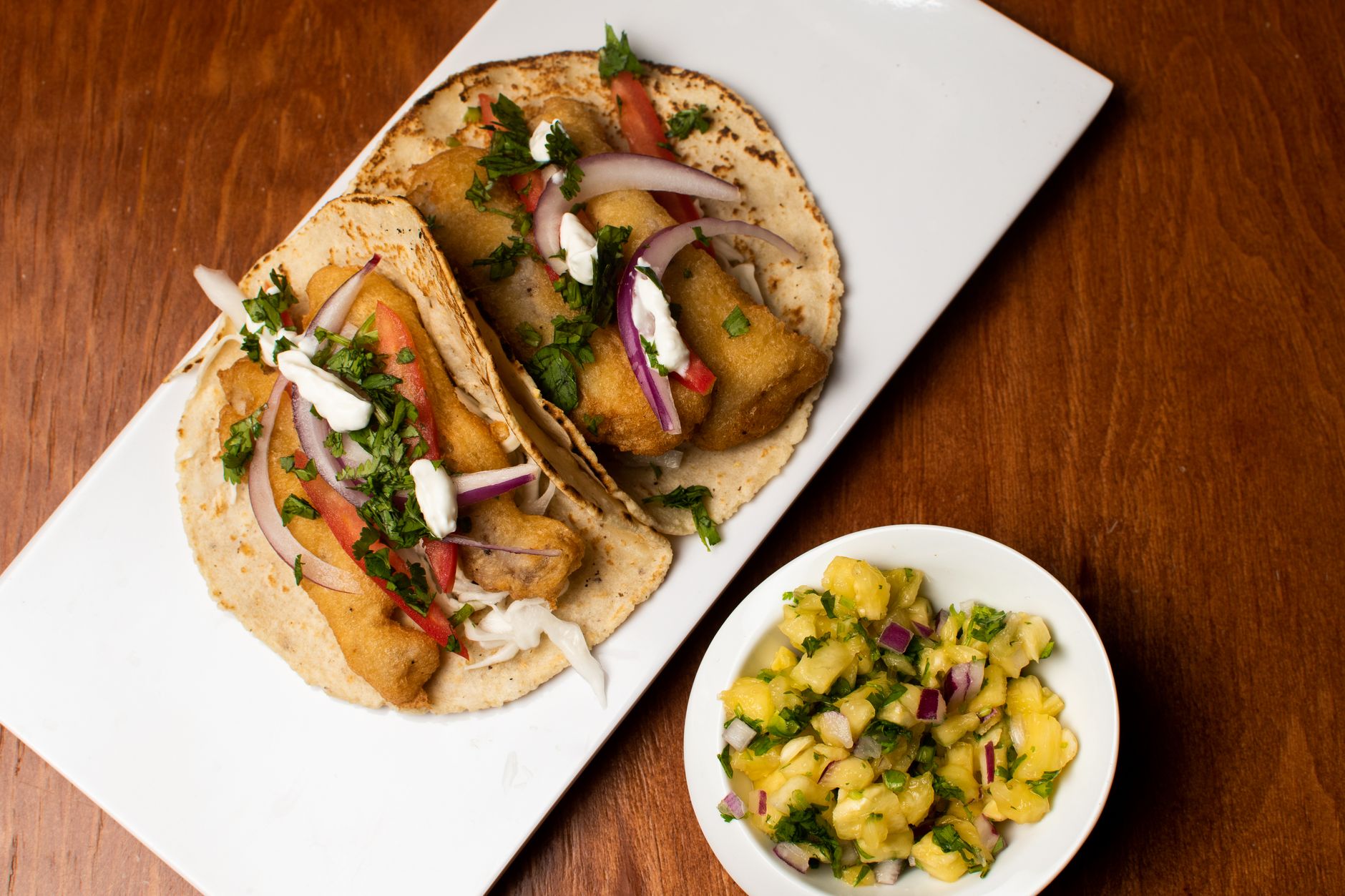 Delicious fish tacos served with fresh pineapple salsa on a wooden surface.