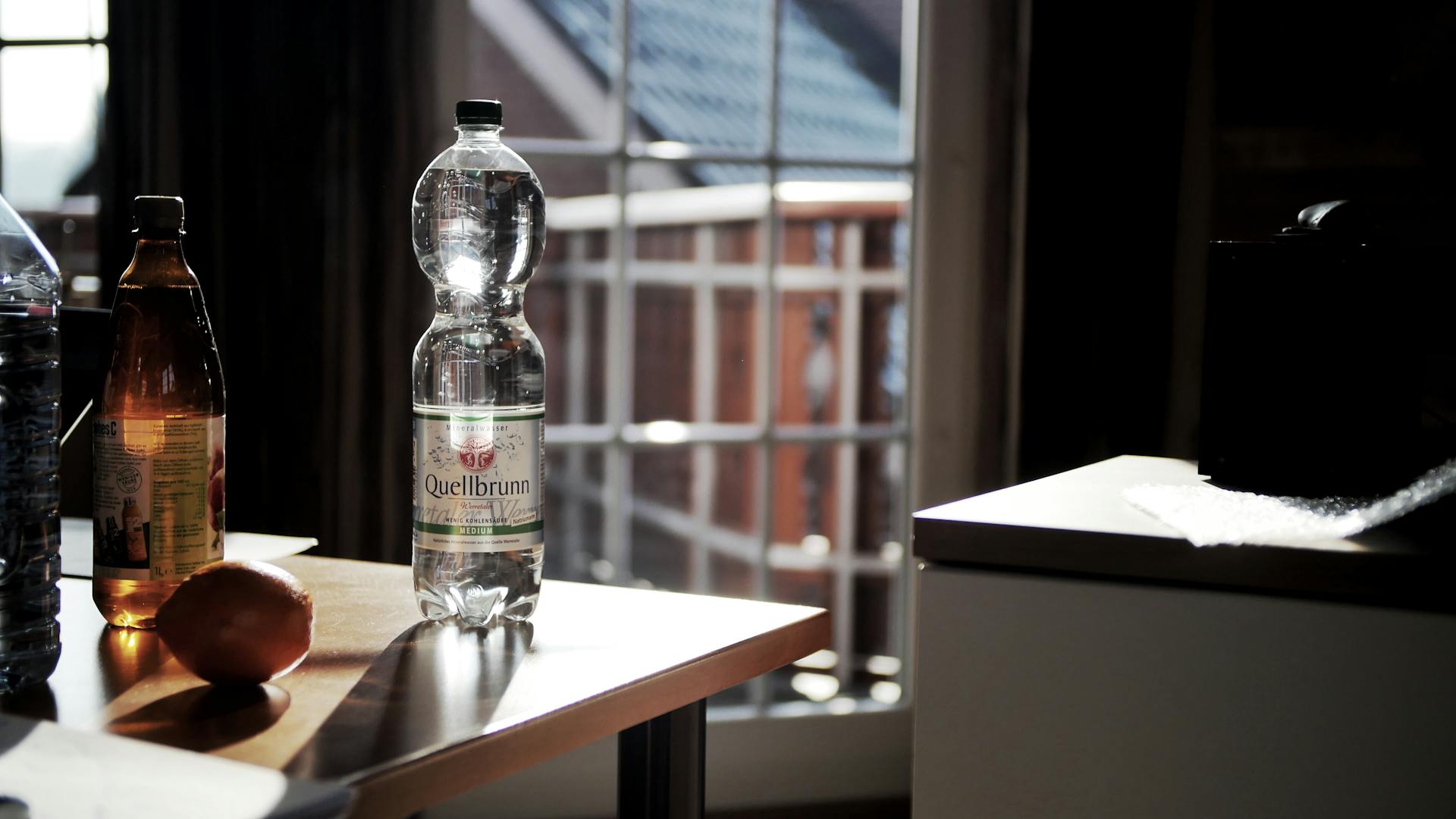 Glass bottles on a sunlit wooden table with a view of a window in a cozy indoor setting.