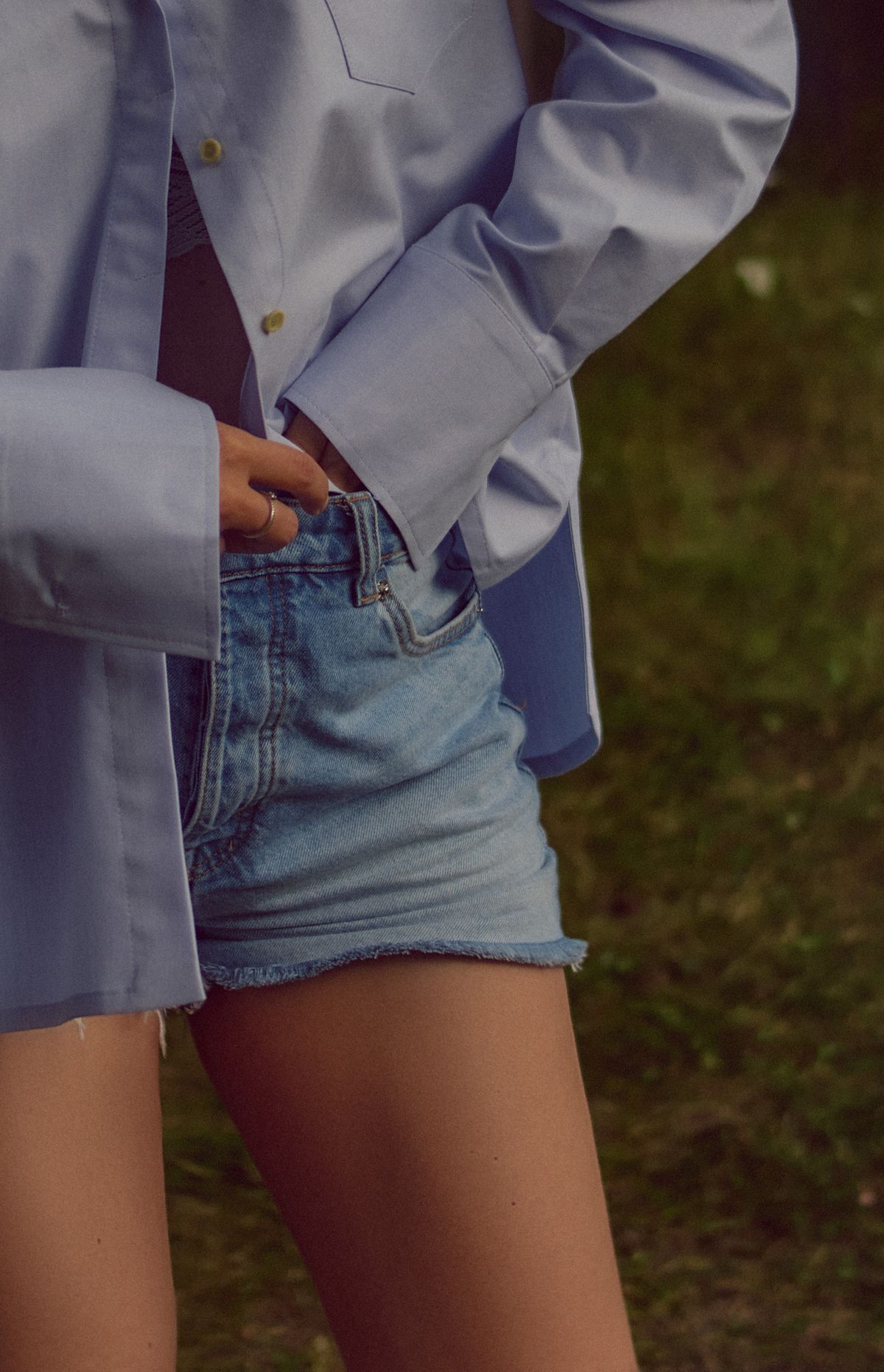 A woman in a blue button-up shirt and denim shorts — the white shirt and denim shorts formula