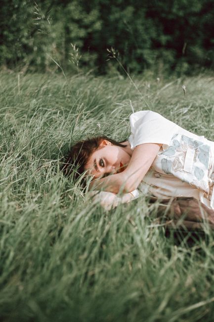 A young woman lying in a peaceful meadow, surrounded by tall grass and a serene natural setting.