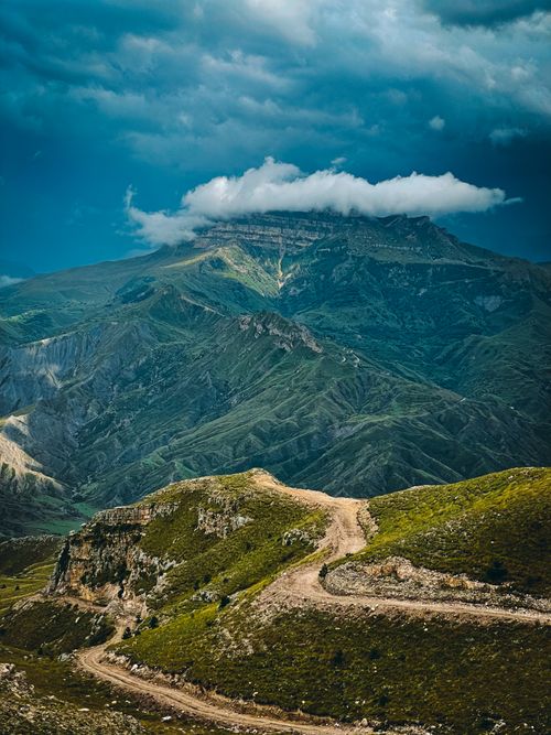 Free Explore a stunning mountain landscape with a winding road leading to magnificent peaks under a dramatic sky. Stock Photo
