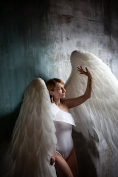 Elegant woman in angel costume with large wings in moody lighting.