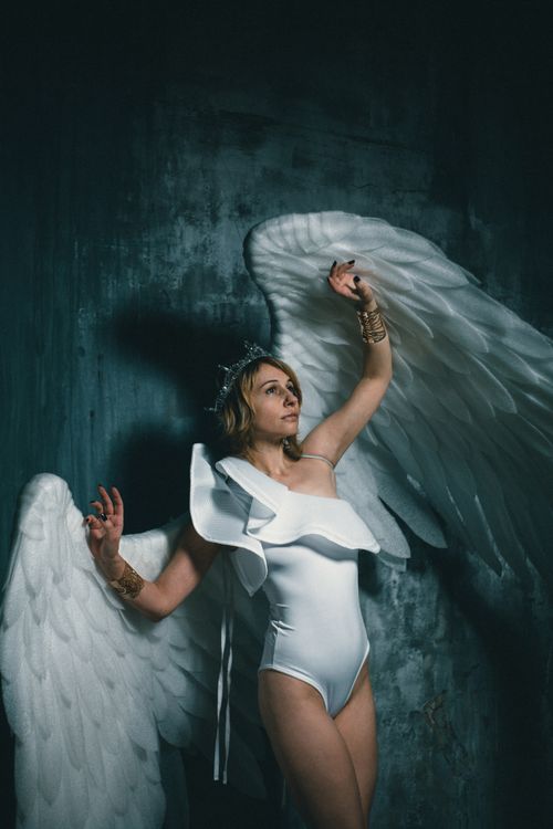 Free A woman in an angel costume poses with raised hands during an indoor photoshoot. Stock Photo