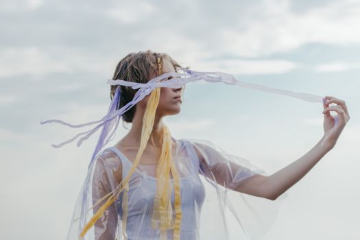 A serene portrait of a woman outdoors with colorful ribbons in a translucent top.