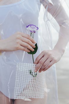 Close-up of a purple flower held by hands through a transparent plastic material against a soft background.