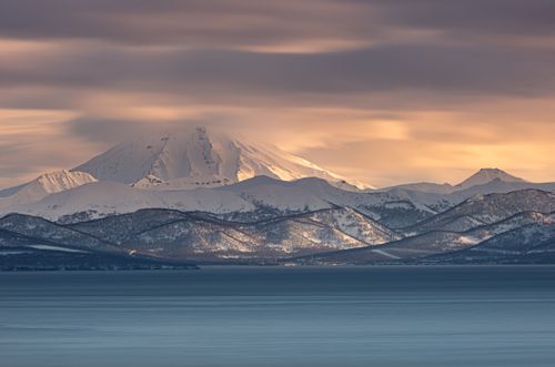 Free Beautiful snow-covered mountain landscape at sunrise with calm waters in the foreground. Stock Photo