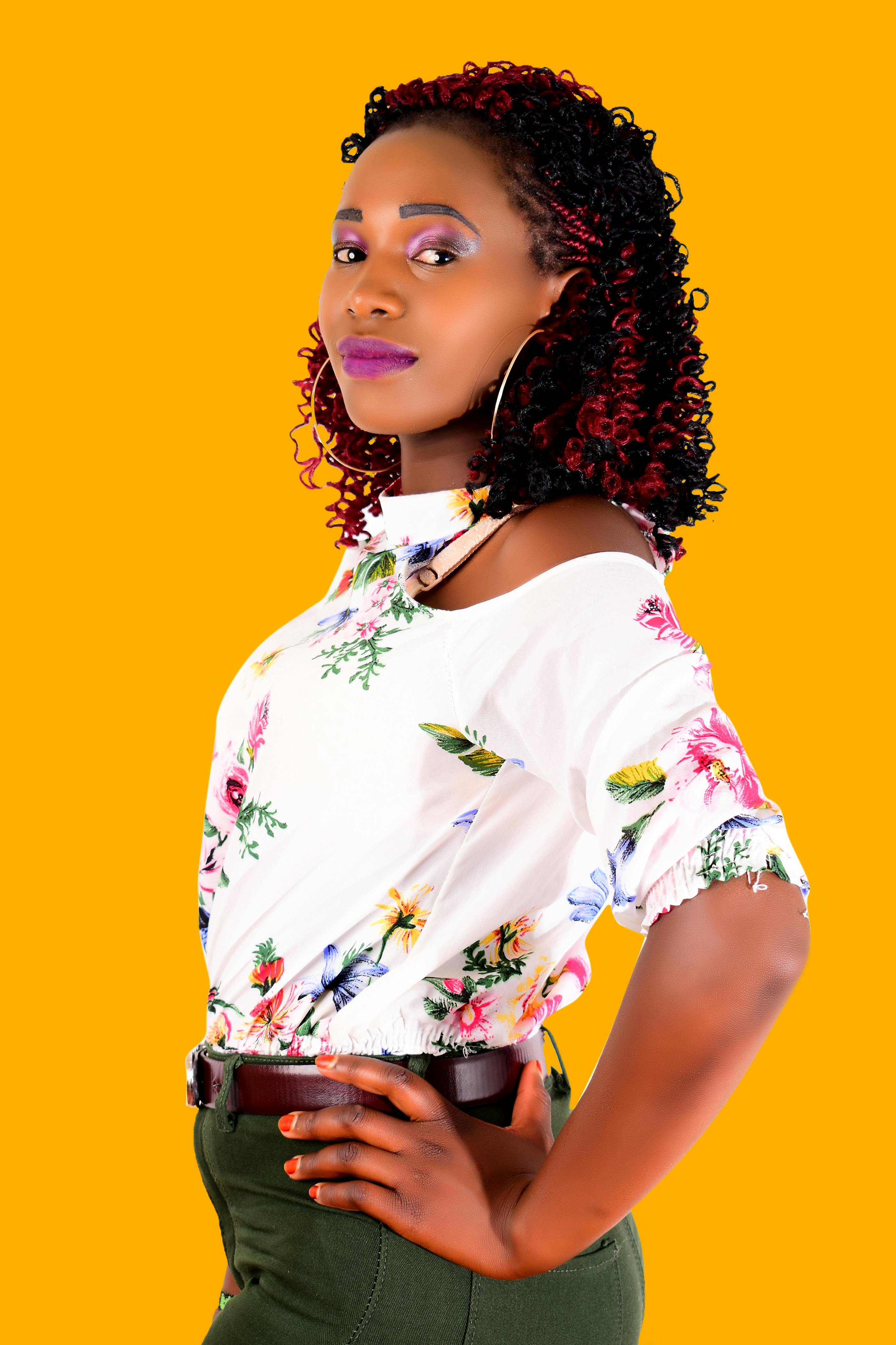 Confident woman in a floral top posing against a vibrant yellow background, exuding elegance and style.