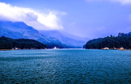 Free Tranquil view of a lake surrounded by lush forests and mountains under a cloudy sky. Stock Photo