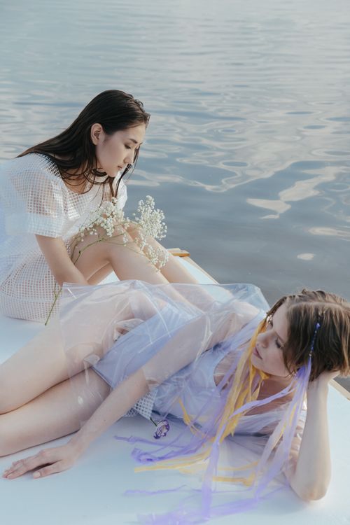 Free Two women relax on a wooden raft by the ocean, enjoying a peaceful day. Stock Photo