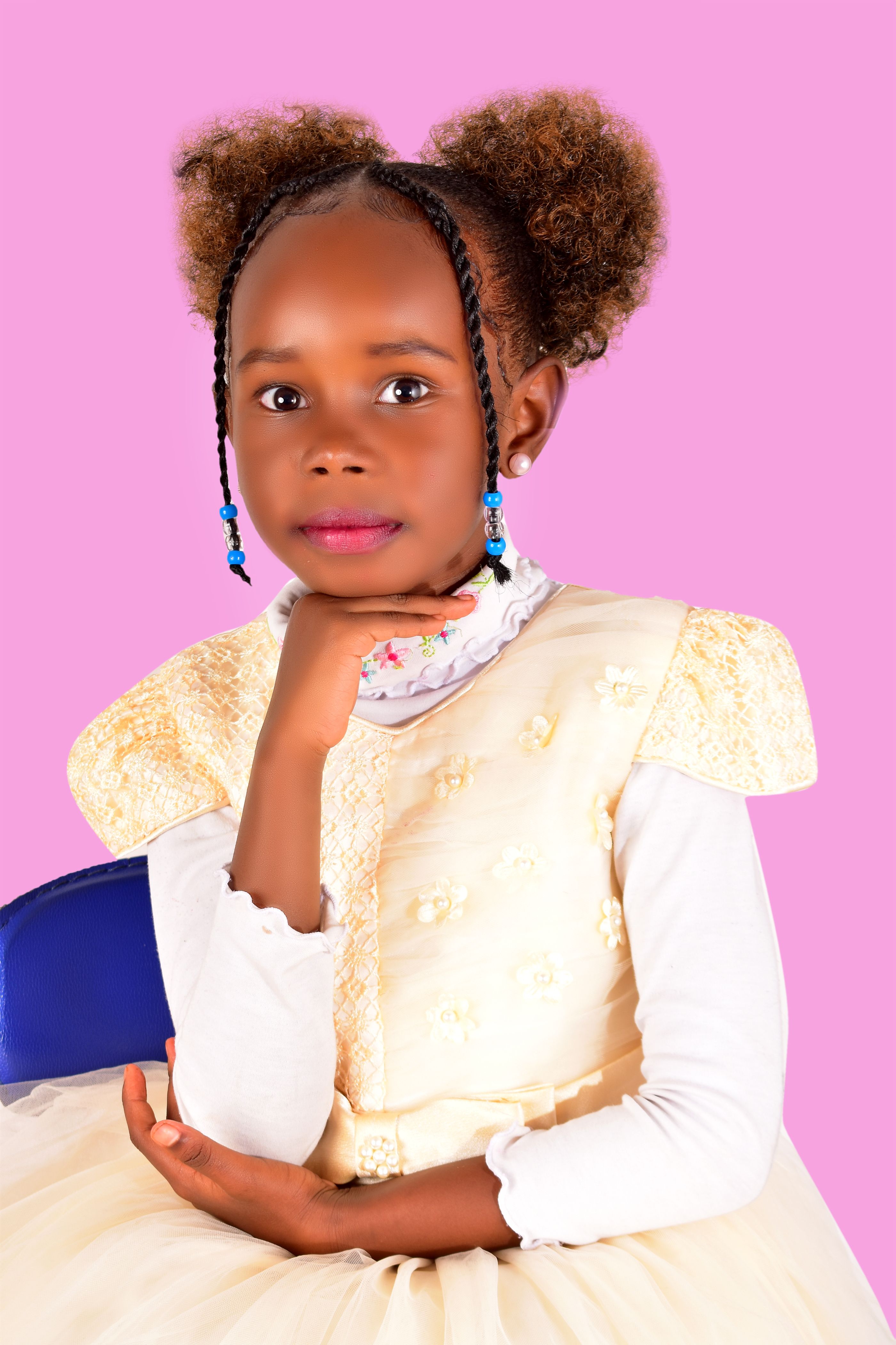 Adorable young girl with braided hair posing with hand on chin against a pink background.