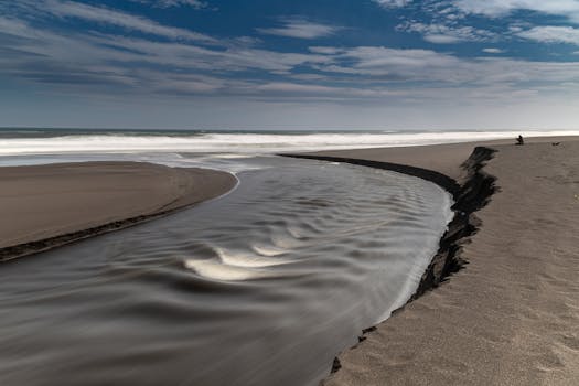 A serene beach scene with dramatic sand erosion and ocean waves under a cloudy sky.
