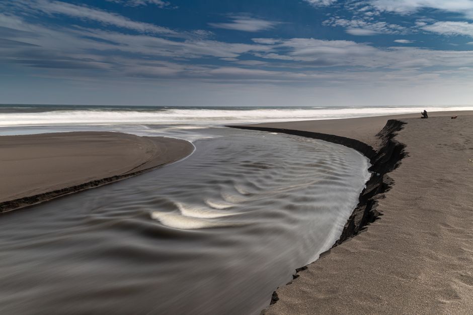 Photo by Александр Максин A serene beach scene with dramatic sand erosion and ocean waves under a cloudy sky.