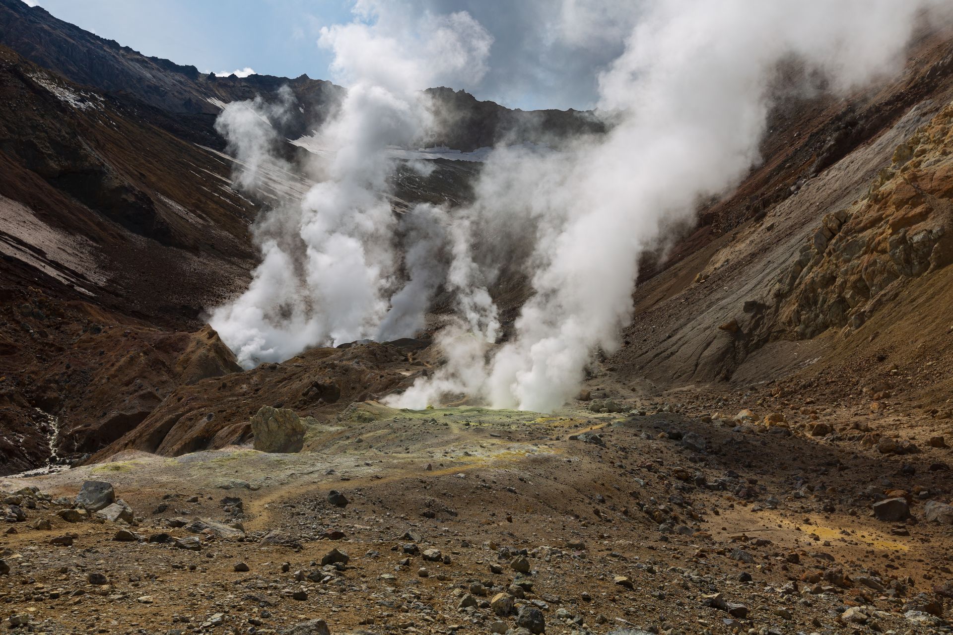 Explore the natural beauty of volcanic steam vents amidst rugged mountains, showcasing geothermal wonders.