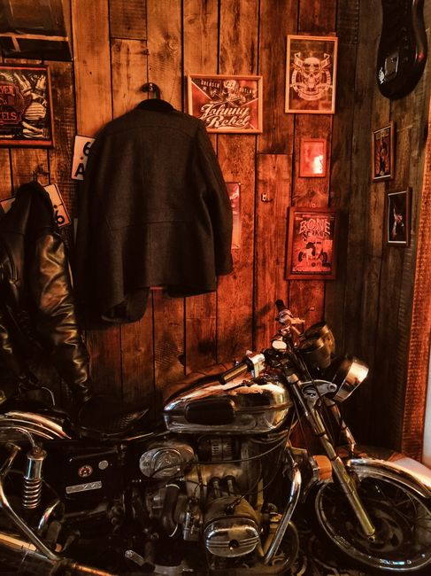 Porte-manteau mural en bois vintage avec motif moto accroché dans un garage ou coin salon, avec casques suspendus et ambiance chaleureuse