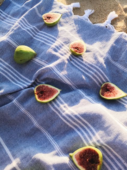 Vertical shot of fresh sliced figs on a blue picnic blanket in sunlight.