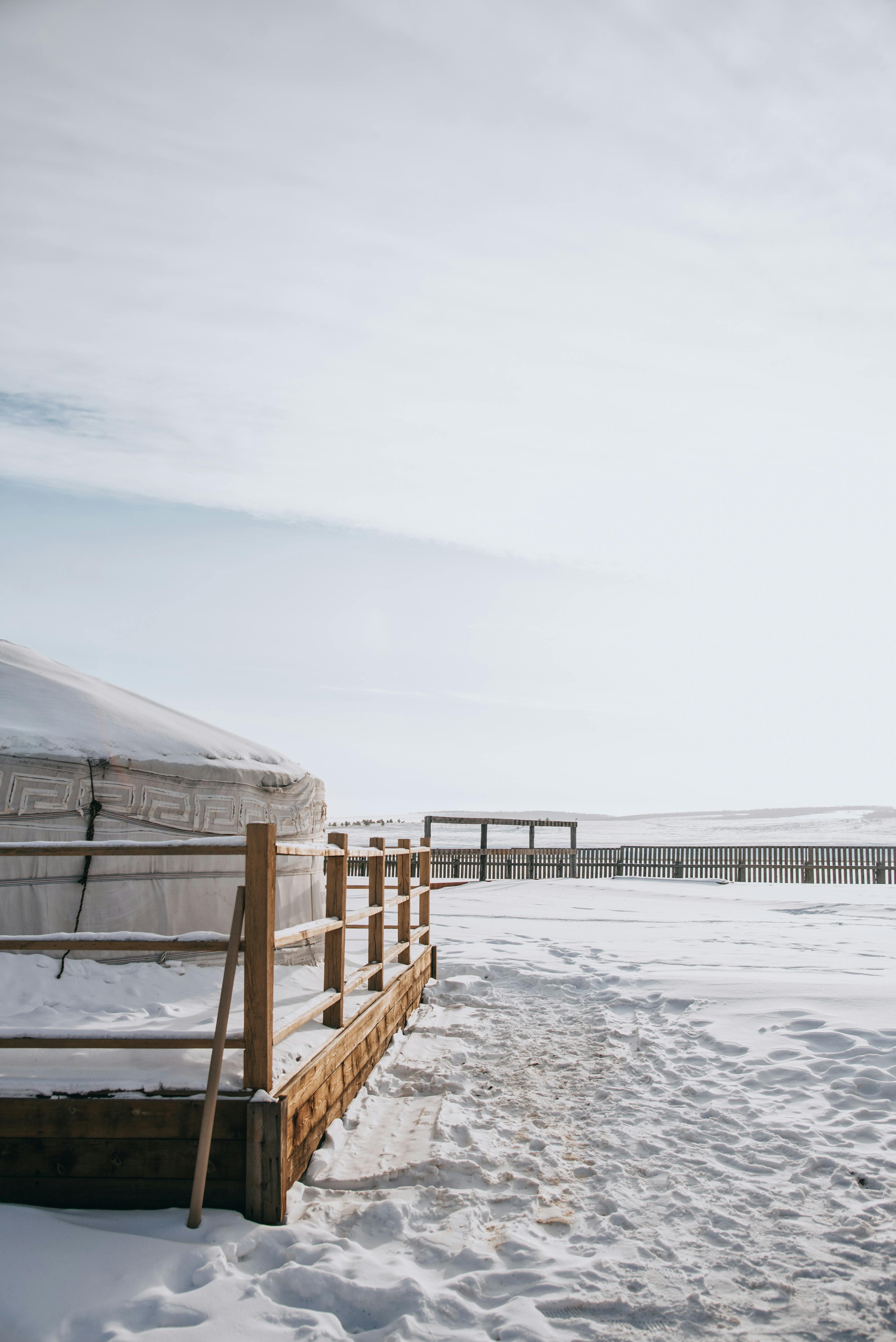 Yurt in a snowy landscape with a wooden fence and clear sky.
