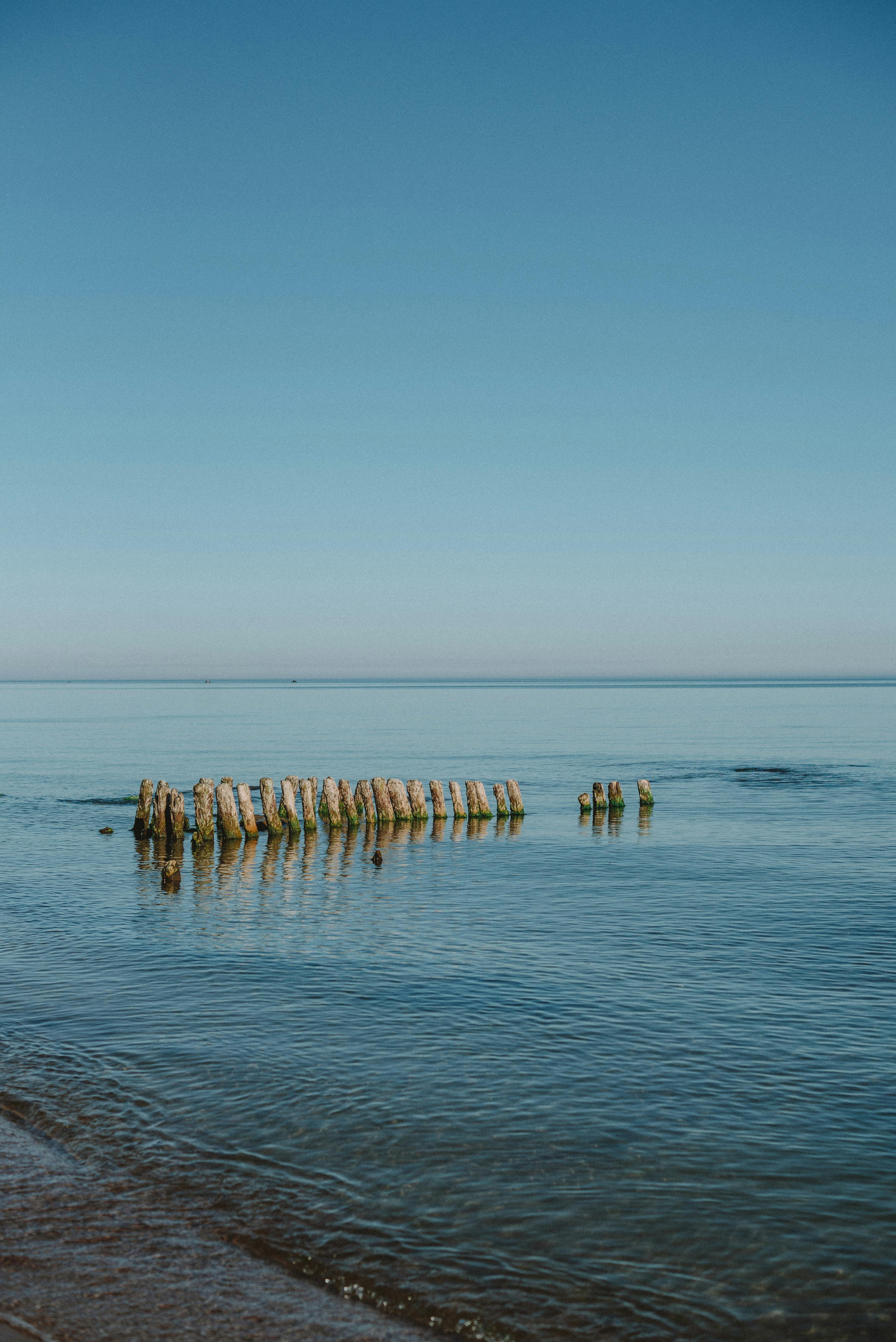 Tranquil ocean scene featuring weathered wooden posts against a clear blue sky, ideal for serene travel themes.