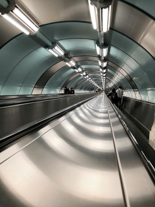 Free A view inside a modern, metallic tunnel with a moving walkway and bright overhead lights, showcasing urban transportation design. Stock Photo