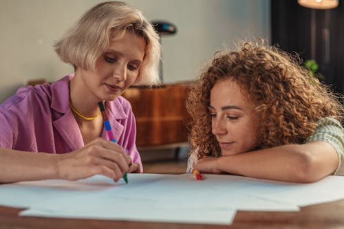 Young Women Sitting at a Table and Drawing on Pieces of Paper