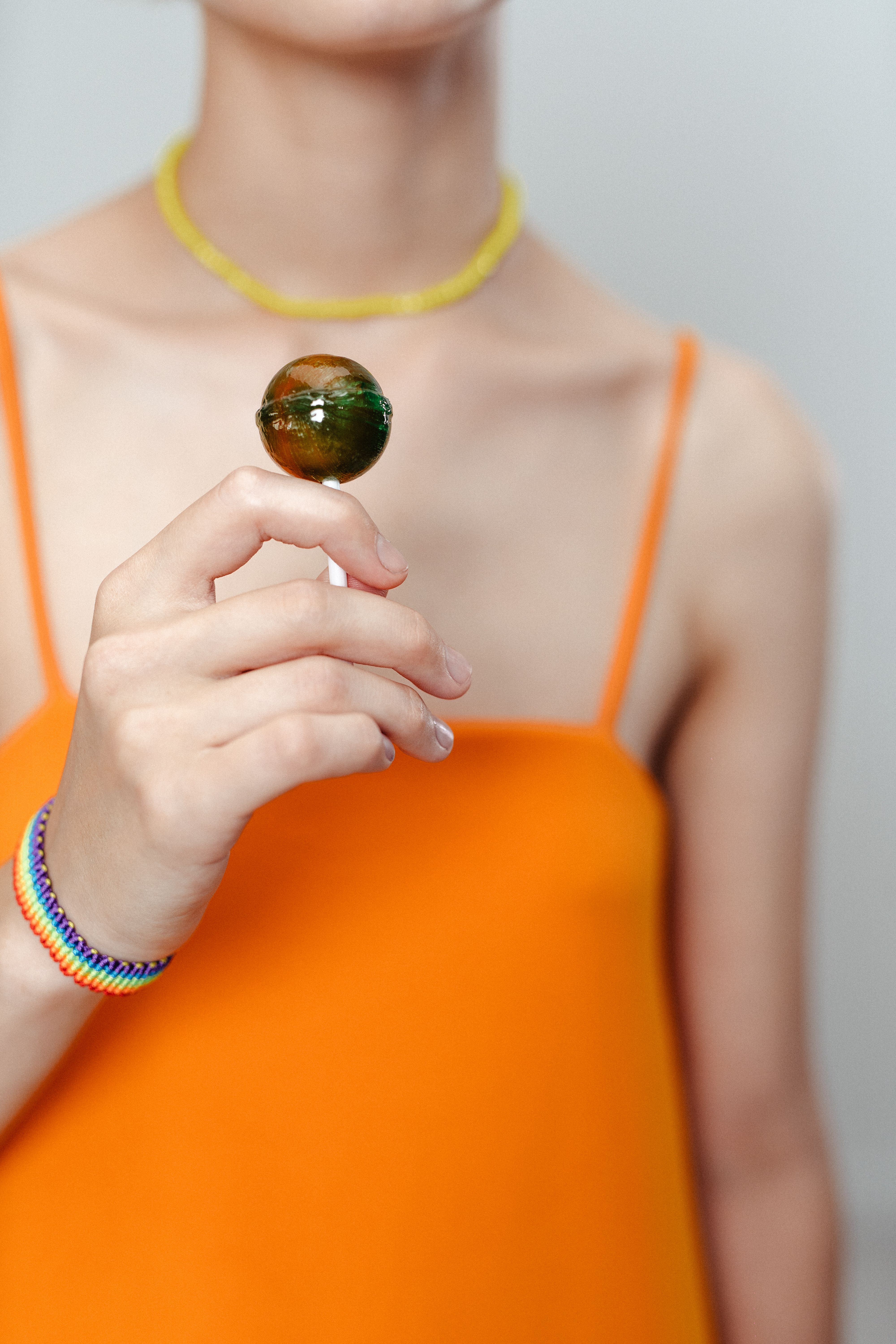 Close-up of a woman holding a vibrant lollipop, dressed in a bright orange top.