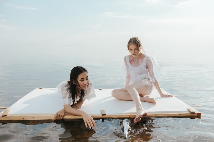 Two Women Sitting On A Wooden Raft On The Ocean