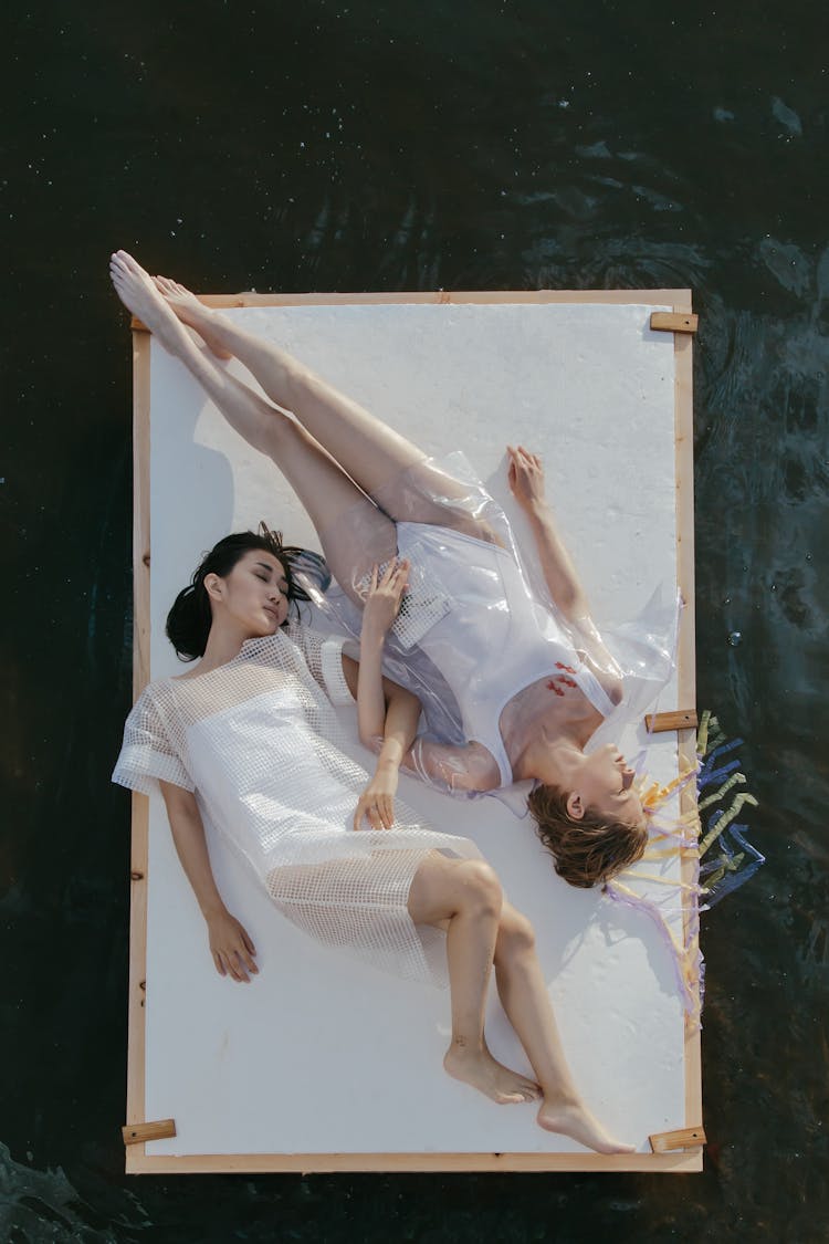 Two Women Lying Down On A Wooden Raft Floating On The Ocean