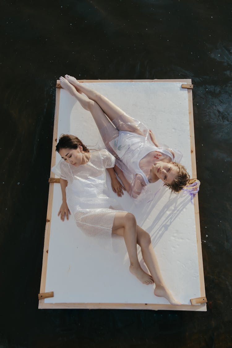 Two Women Lying Down On A Wooden Raft Floating On The Ocean