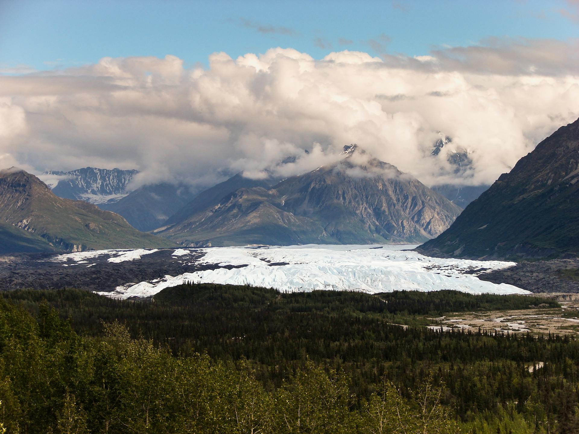 Breathtaking view of Alaskan snow-covered mountains and glacier under cloudy skies.