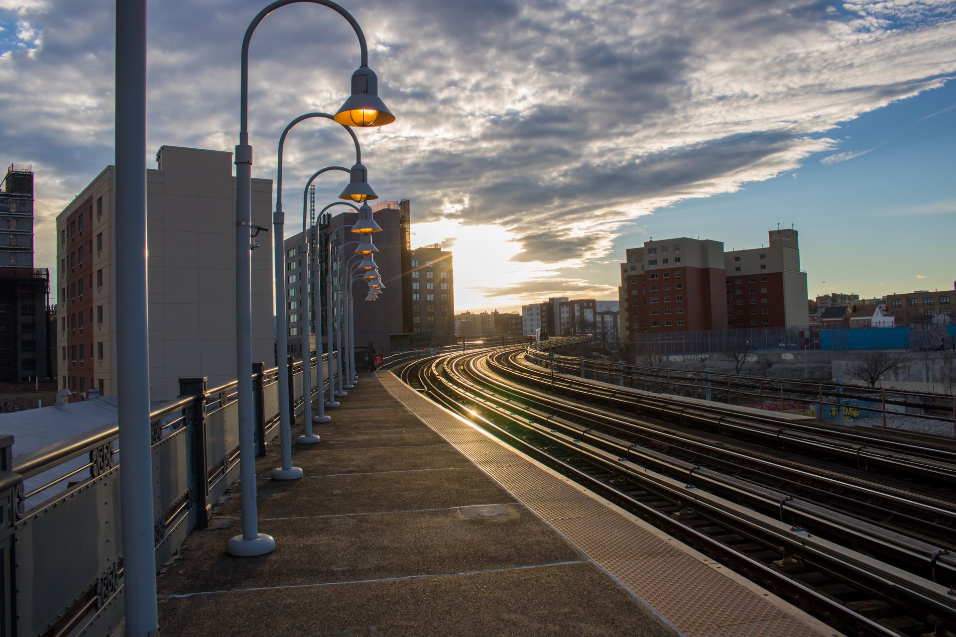 Sunset view of an urban train station platform with lamp posts and rails.