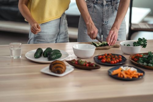 Free Two people preparing a healthy vegetarian meal with fresh vegetables and snacks on a wooden table. Stock Photo