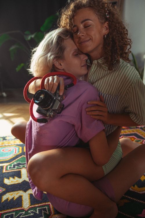 Free A warm embrace between two women sitting on a colorful rug, captured in a cozy indoor setting. Stock Photo