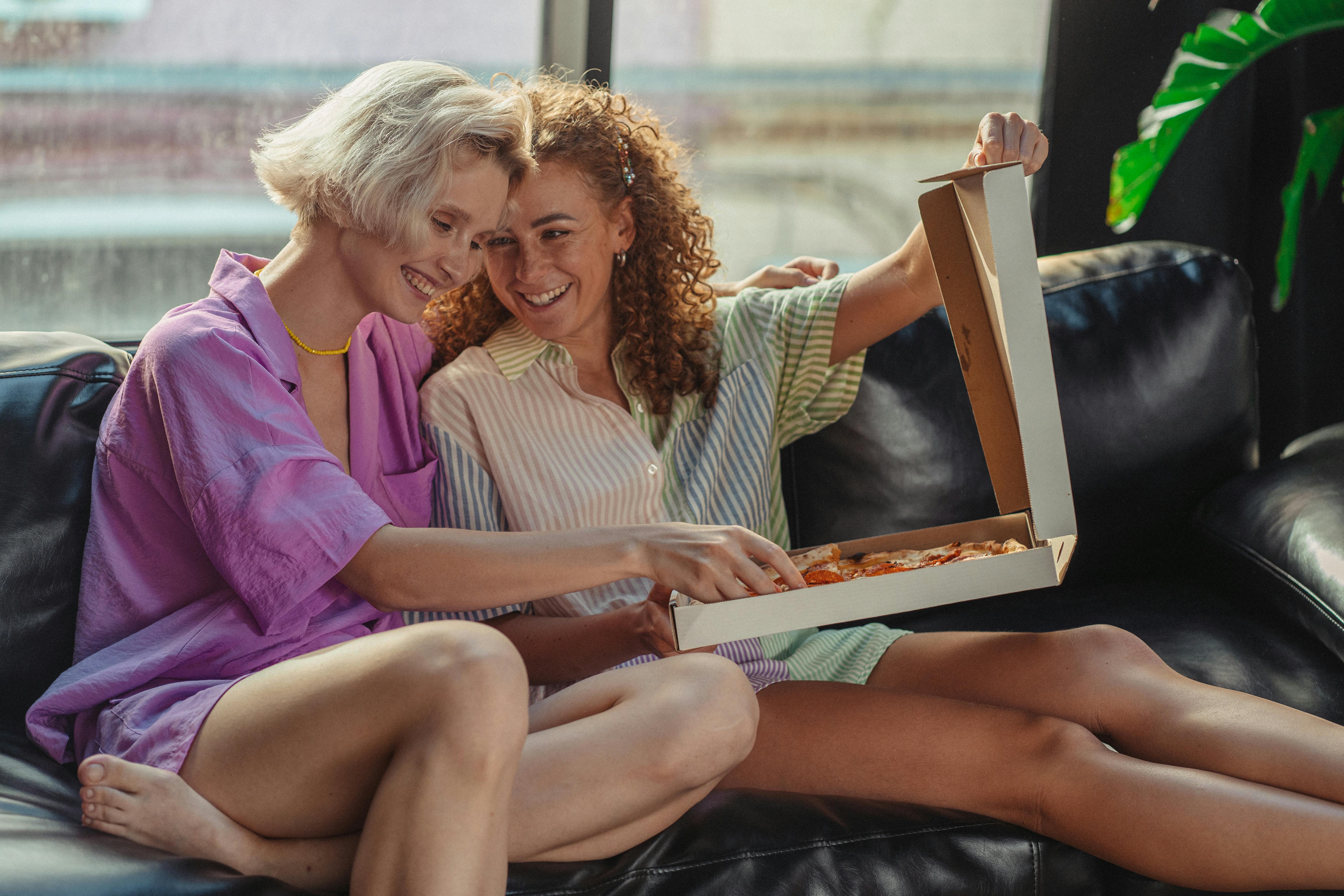 women sharing a box of pizza on a couch