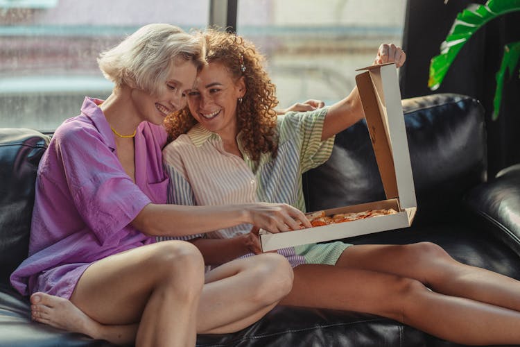 Women Sharing A Box Of Pizza On A Couch