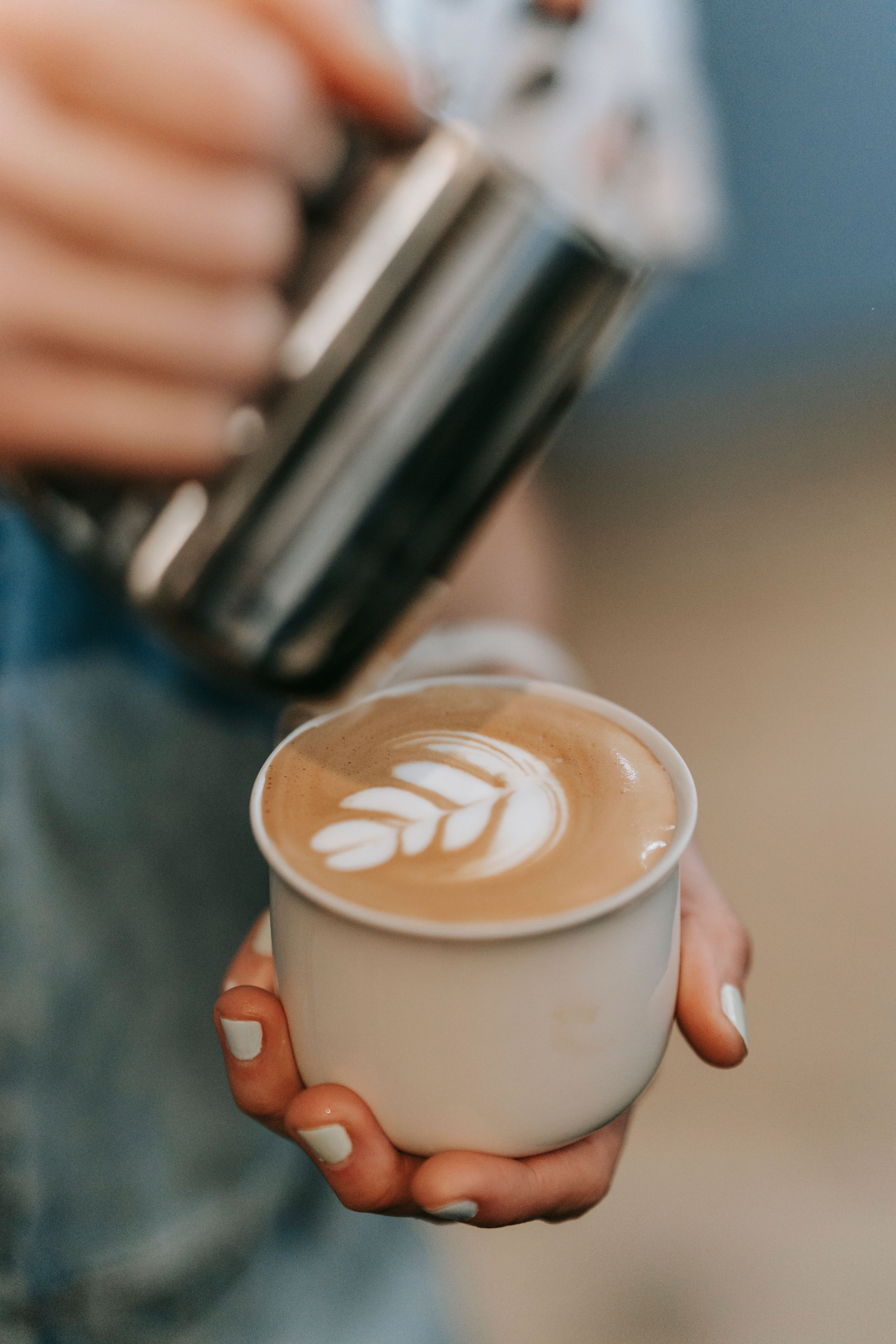 Hands holding a cappuccino with heart latte art, wrapped for a Chiang Rai morning