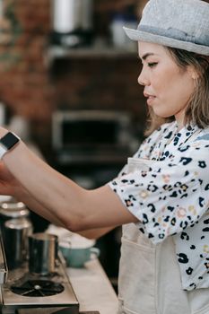 Asian female barista making espresso at a coffee shop, showcasing precision and dedication.