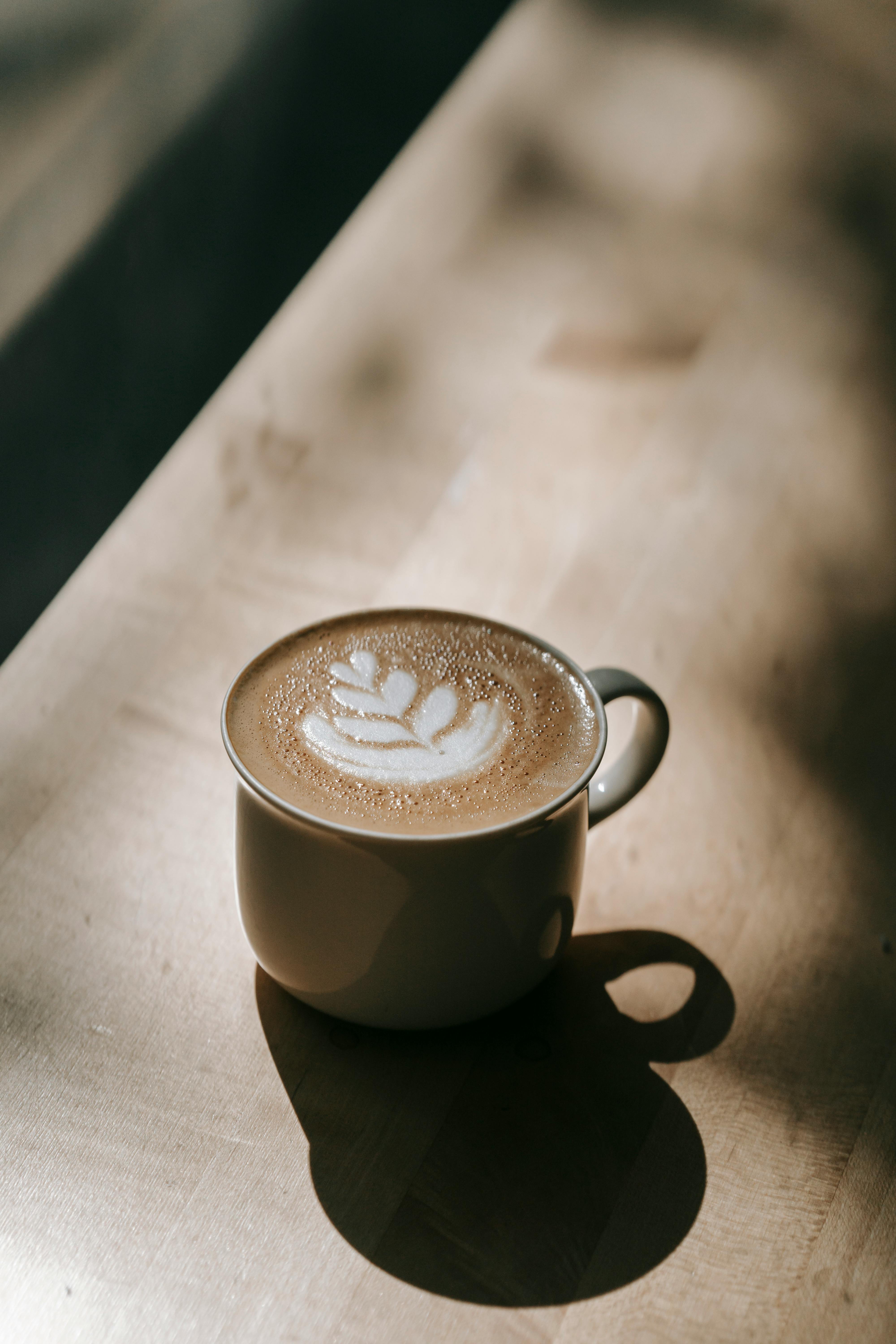 A beautiful cup of latte with art design, bathed in warm sunlight on a wooden table.