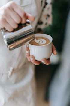 A barista carefully pours latte art into a steaming cup in a cozy cafe.