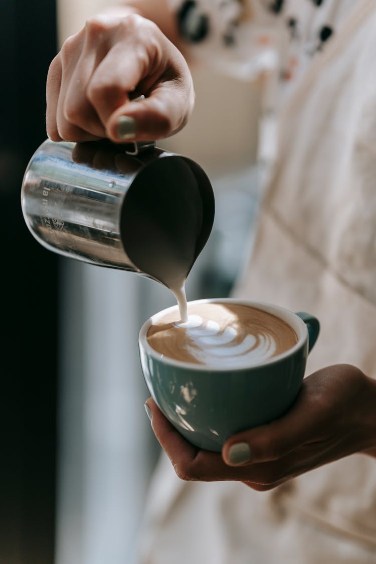 Close-Up Shot Of A Person Pouring Cream Of Latte On A Cup Of Cappuccino