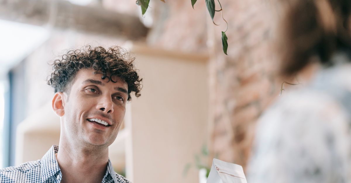 Casual indoor scene of a smiling man with curly hair conversing happily.