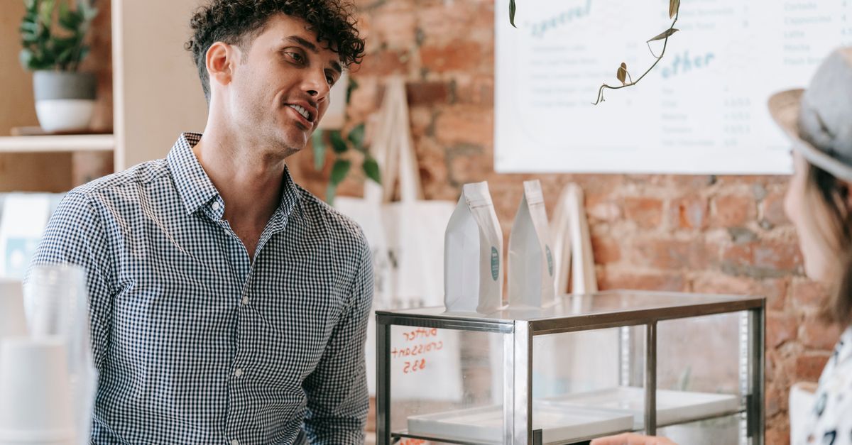 A person smiling at a stranger in a coffee shop queue, warm lighting