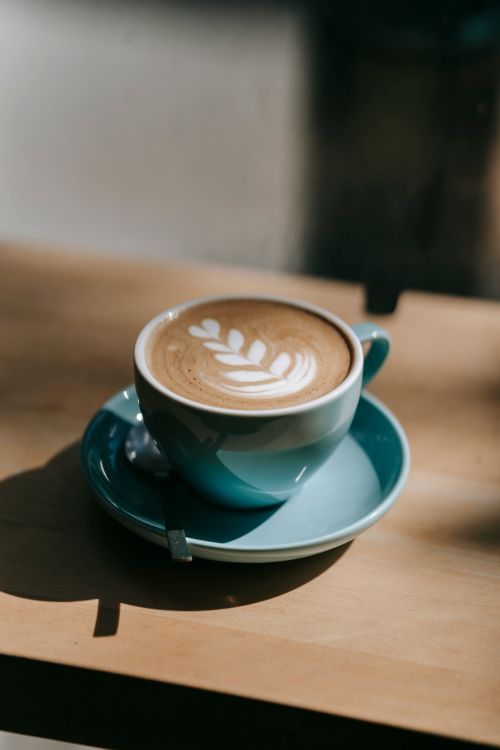 Free Close-up of a cappuccino with leaf latte art in a blue cup on a wooden table. Stock Photo