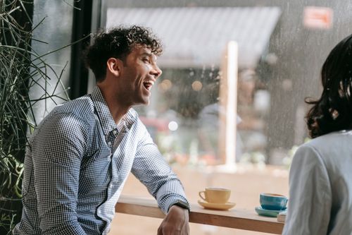 Free A man in smart casual attire laughs while sitting in a café, enjoying the moment. Stock Photo