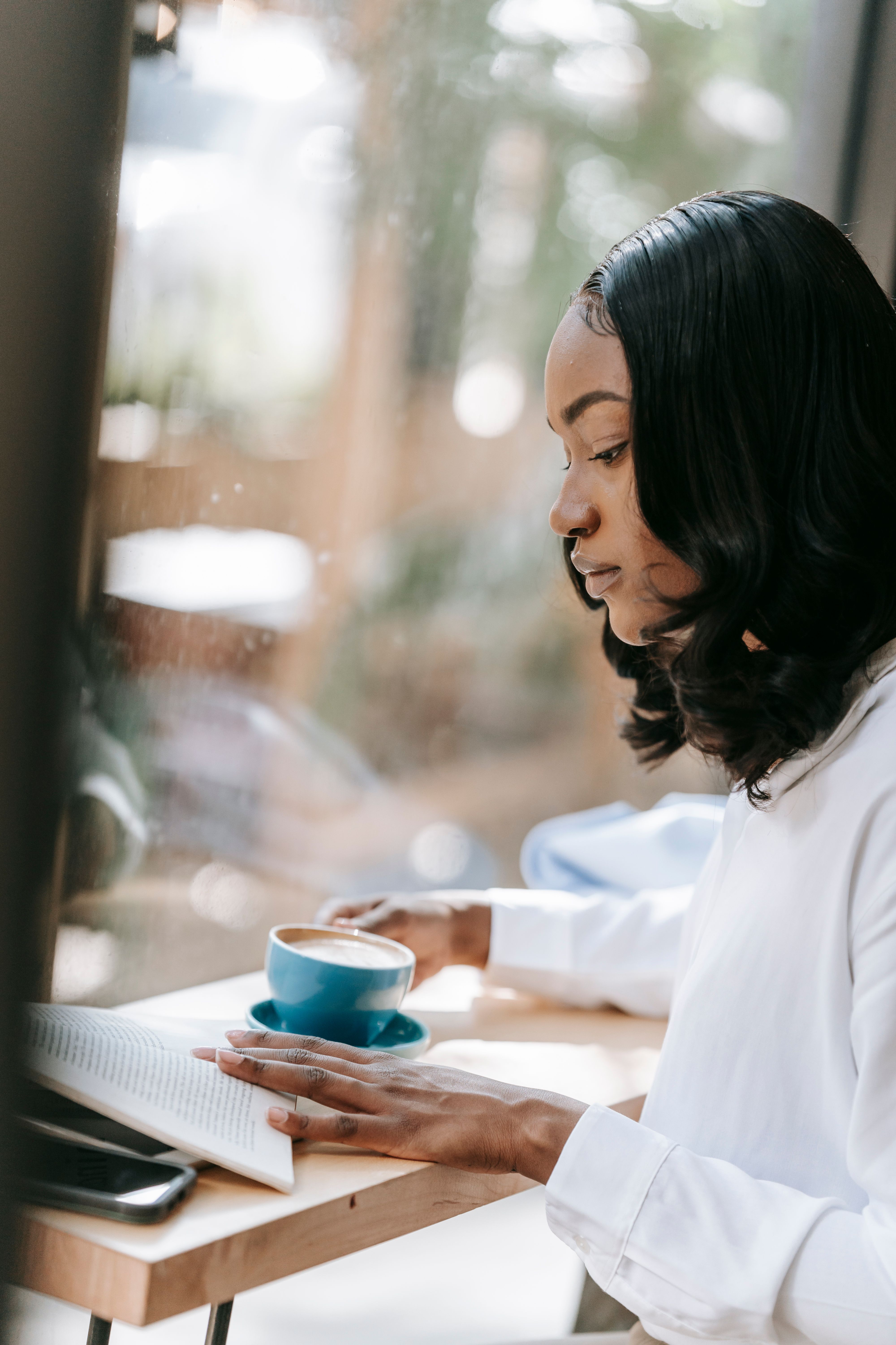 Young woman enjoying a coffee and reading by the window. Perfect for lifestyle themes.