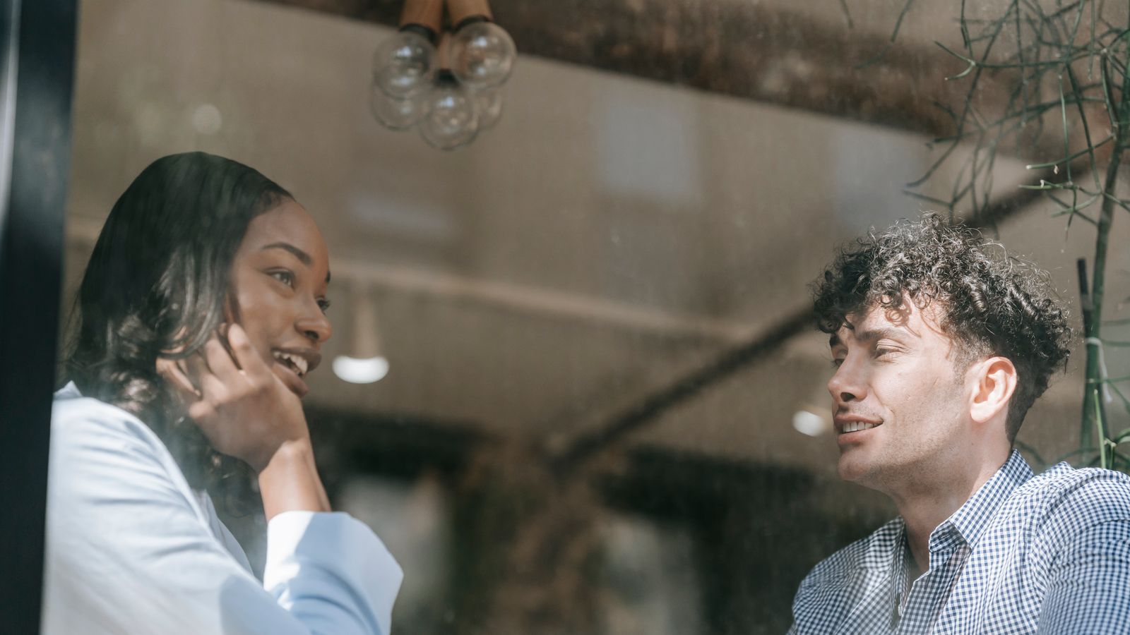 Two people having an animated conversation over coffee, seen through a window