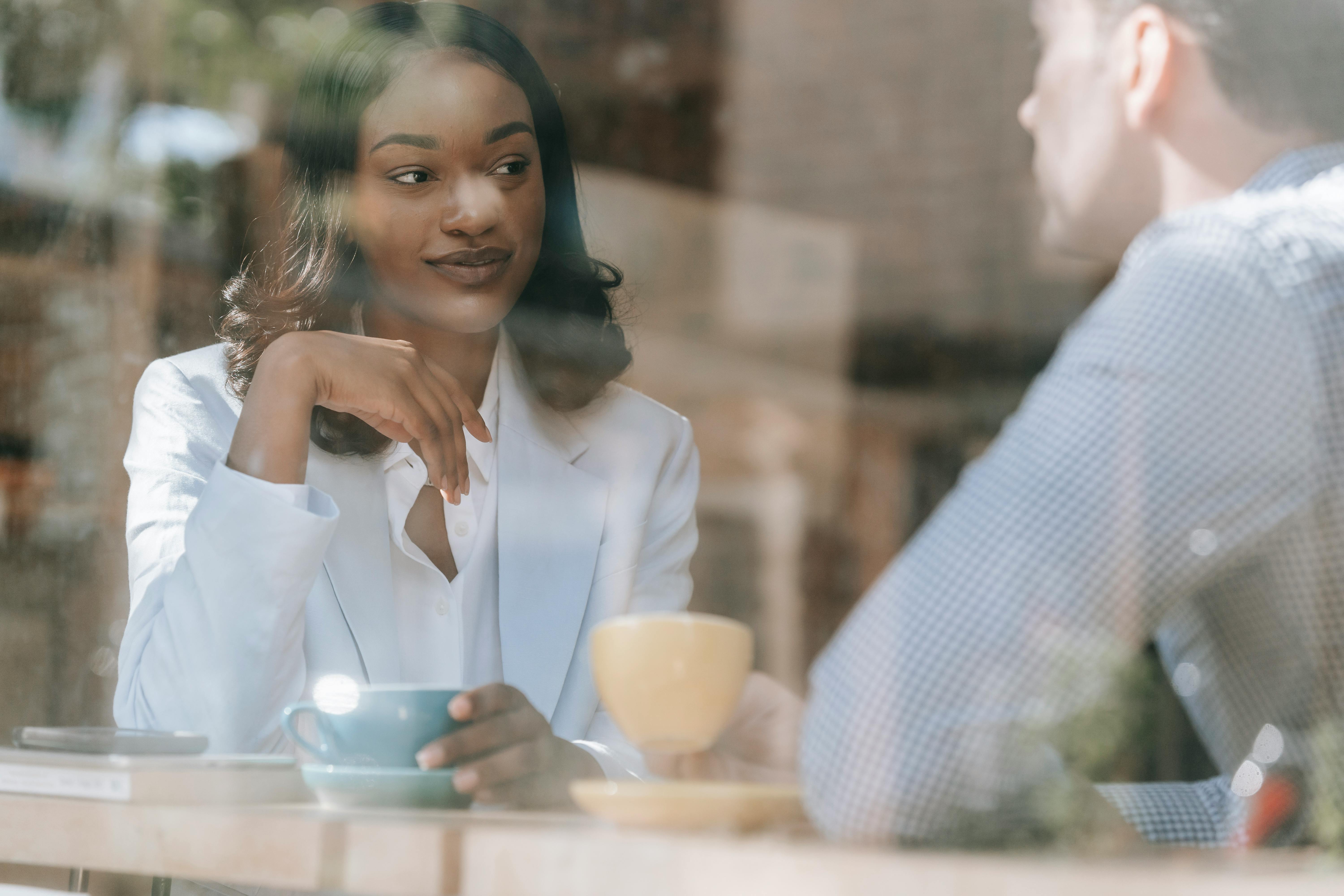 Two adults enjoy a friendly conversation over coffee in a sunlit cafe.