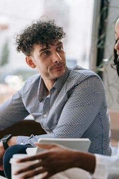 Two adults conversing in a café, focusing on technology and communication.