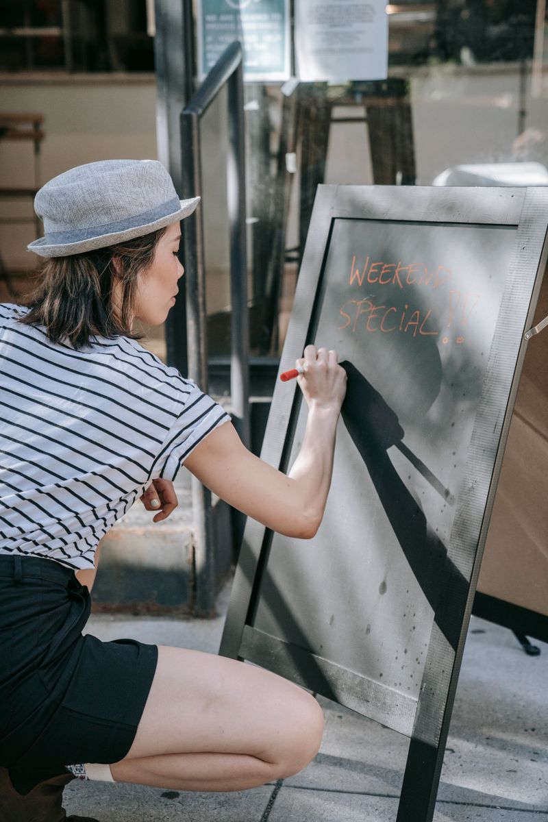Woman in a hat and striped shirt writing 'weekend special' on a cafe chalkboard outside.