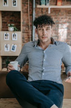 Confident man sitting with coffee in a relaxed office environment, showing a smart casual style.